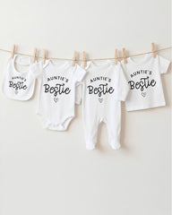 A row of white baby clothes with the text "Auntie's Bestie" printed on them, along with a bib and a pair of white onesies.