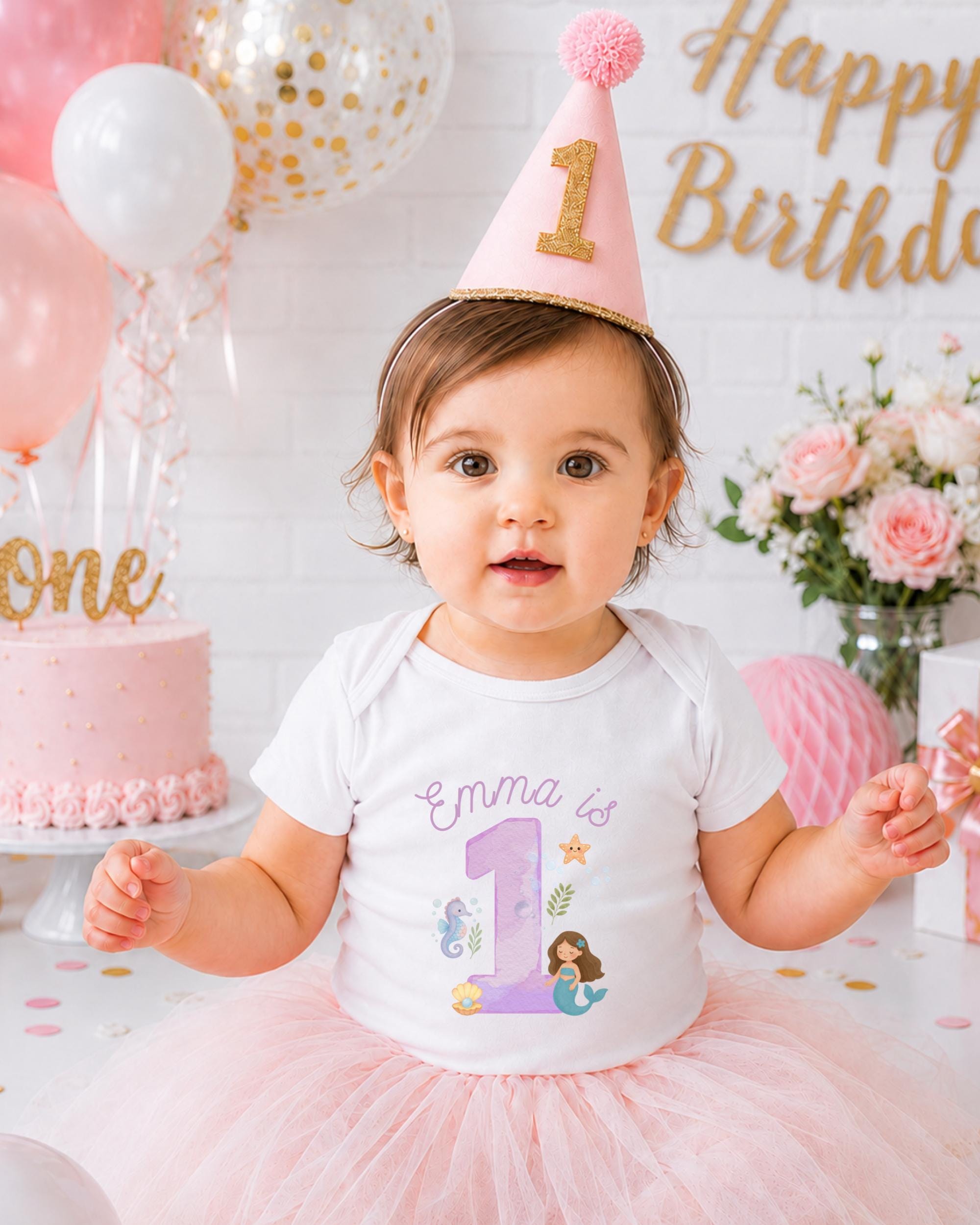 A young girl wearing a pink party hat and a white t-shirt with a mermaid design is posing for a birthday photo.