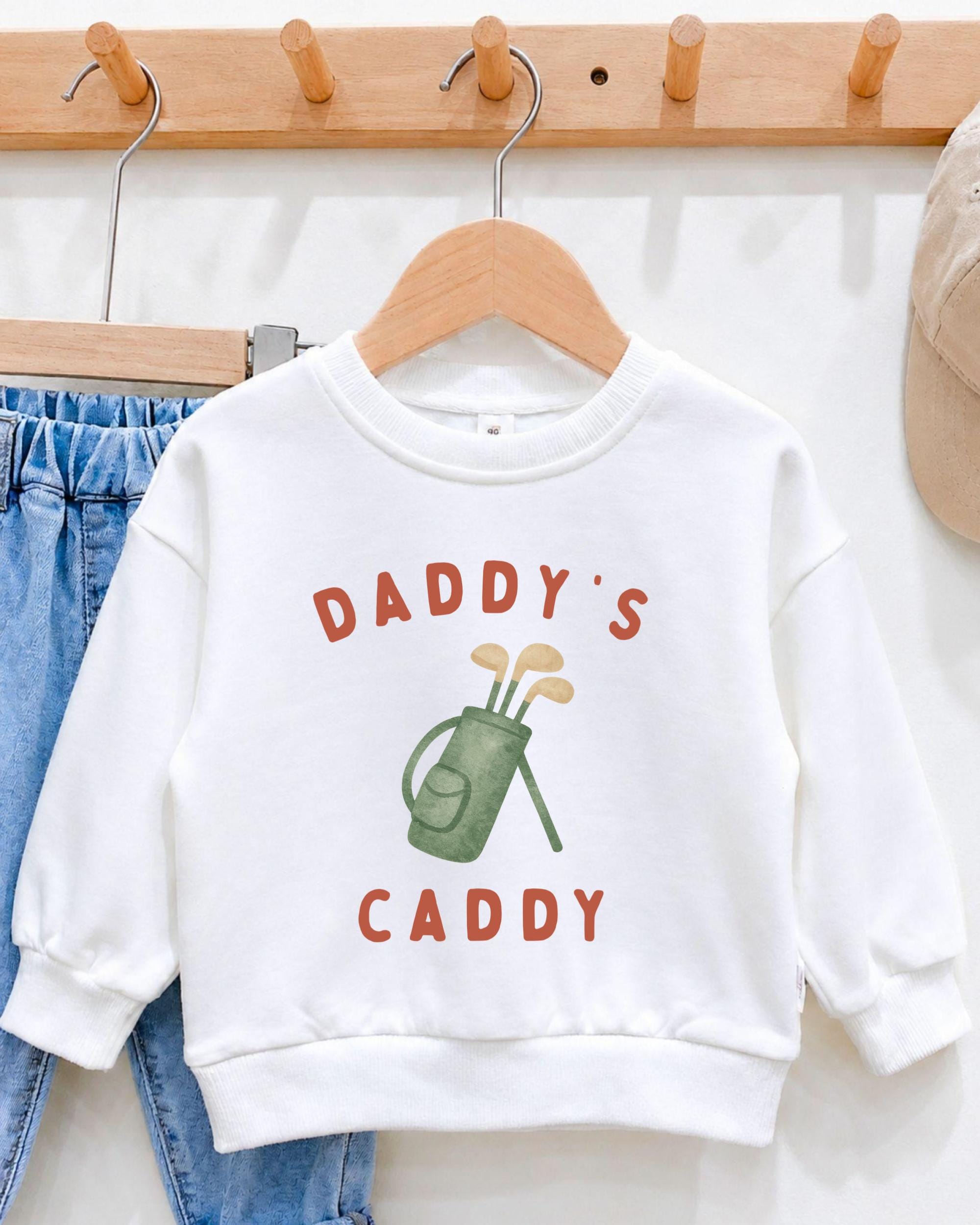 A white sweatshirt with the text "DADRY'S CADDY" printed on it, along with an illustration of a golf club and bag.