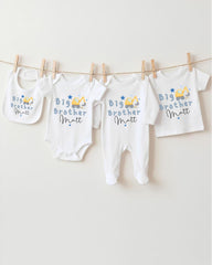 A row of four white baby clothes with the text "Big Brother Matt" printed on them, hanging on a clothesline.