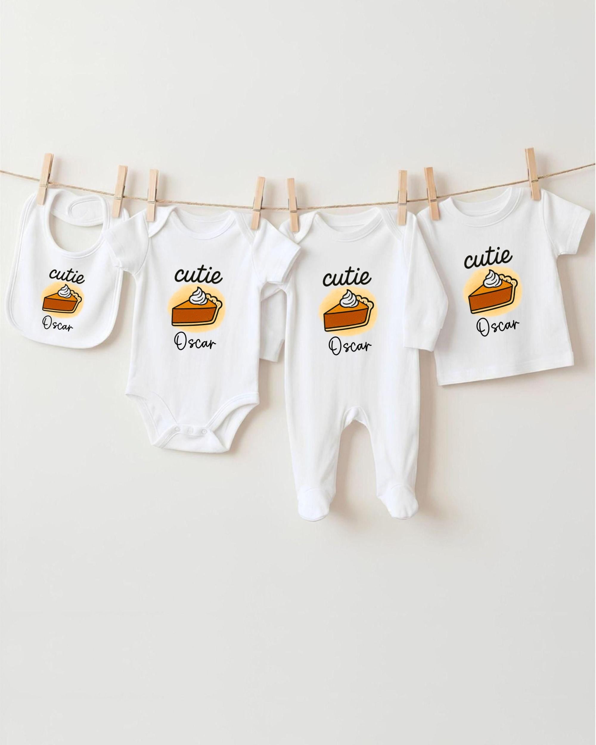 A row of four white baby clothes with the name "Oscar" printed on them, hanging on a clothesline.