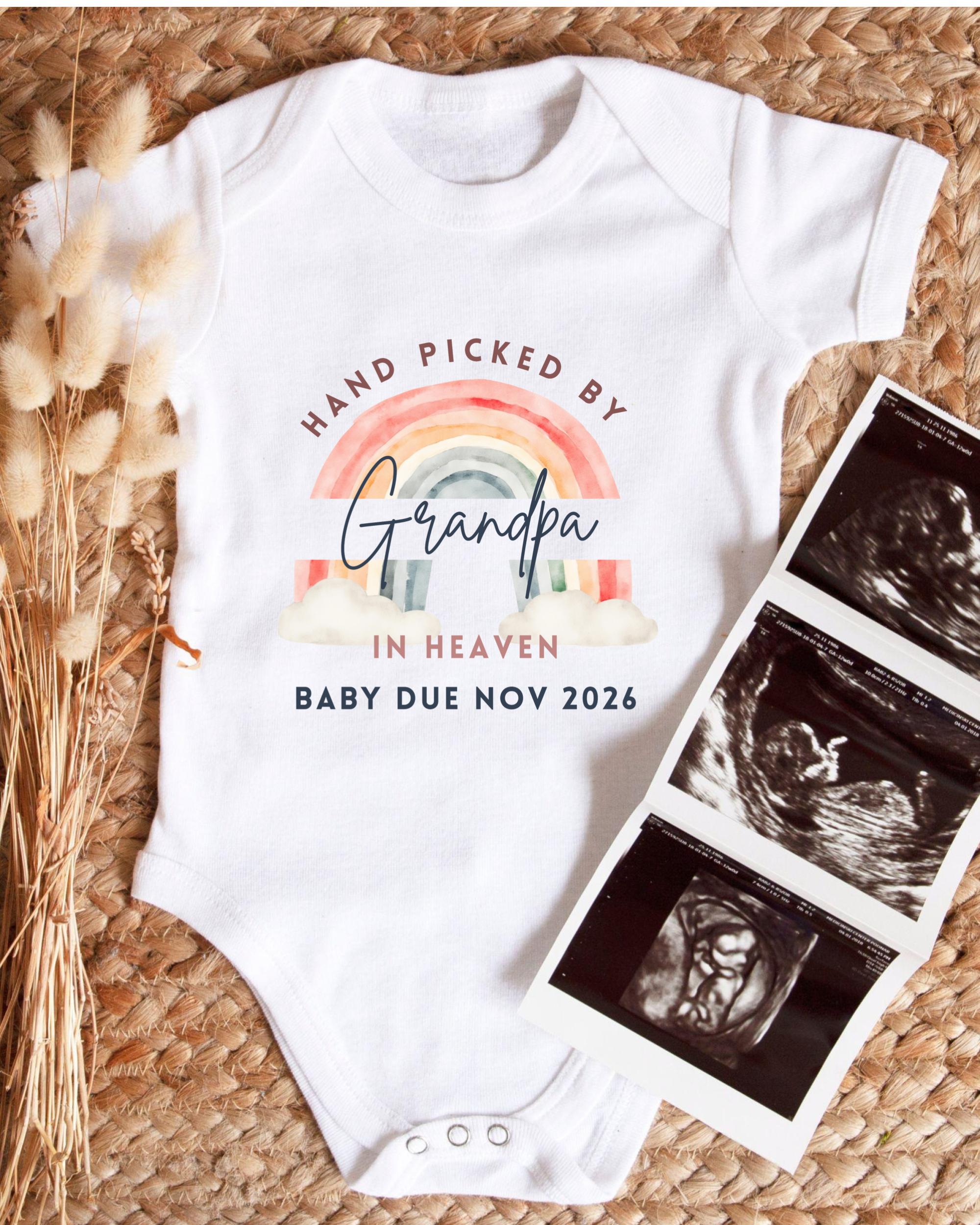 A white baby onesie with a rainbow graphic and text that says "Hand picked by Grandpa in Heaven" and "Baby due Nov 2026". Next to the onesie is a set of three black and white baby ultrasound images.