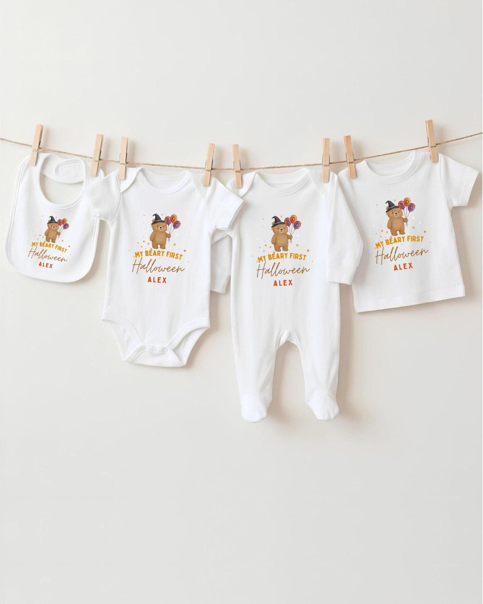 A row of four white baby clothes with Halloween-themed designs hanging on a clothesline.