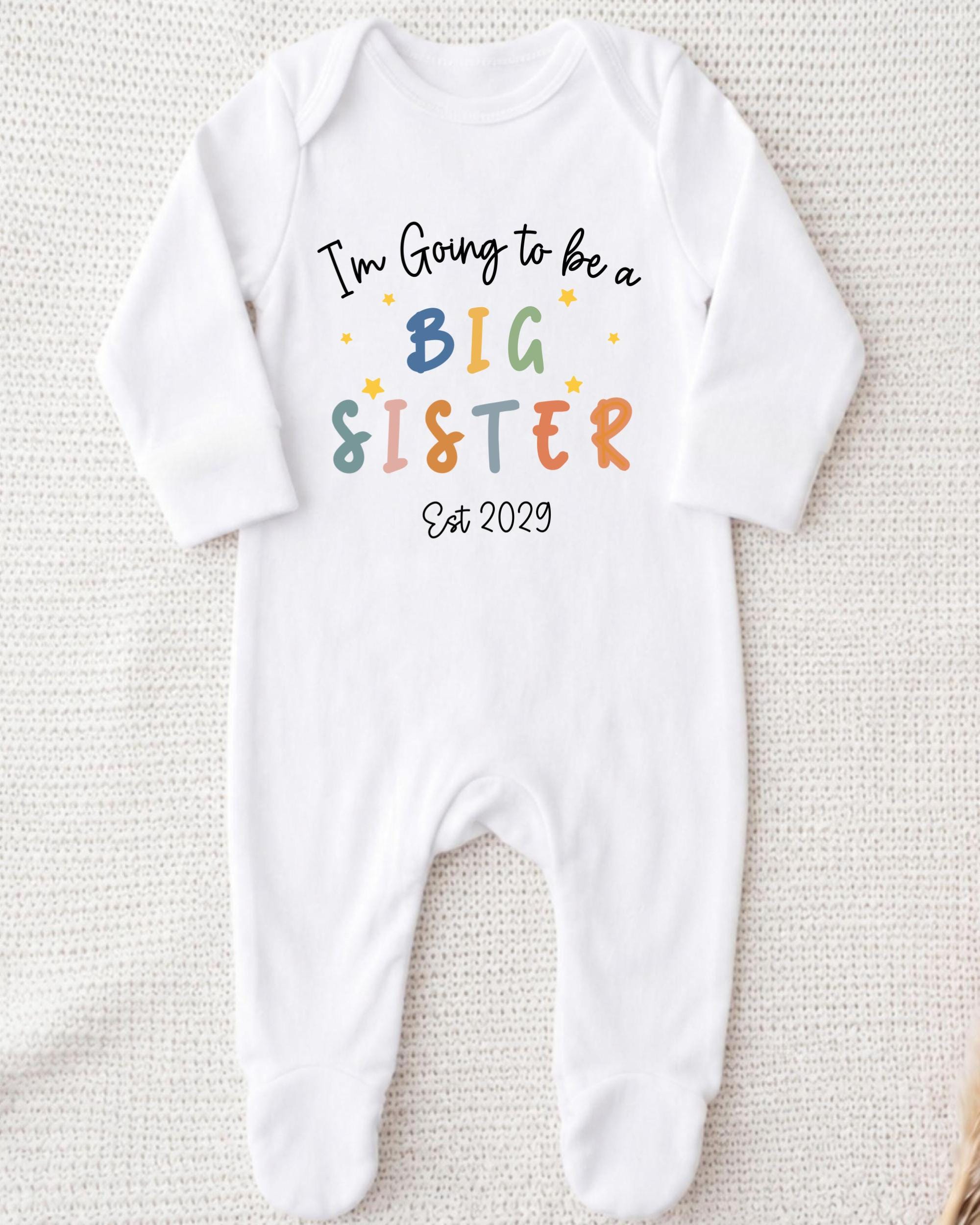 A white onesie with text that says "I'm going to be a big sister" printed on it.