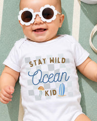 A smiling baby wearing a white onesie with a graphic design and text, lying on a green and white striped surface.