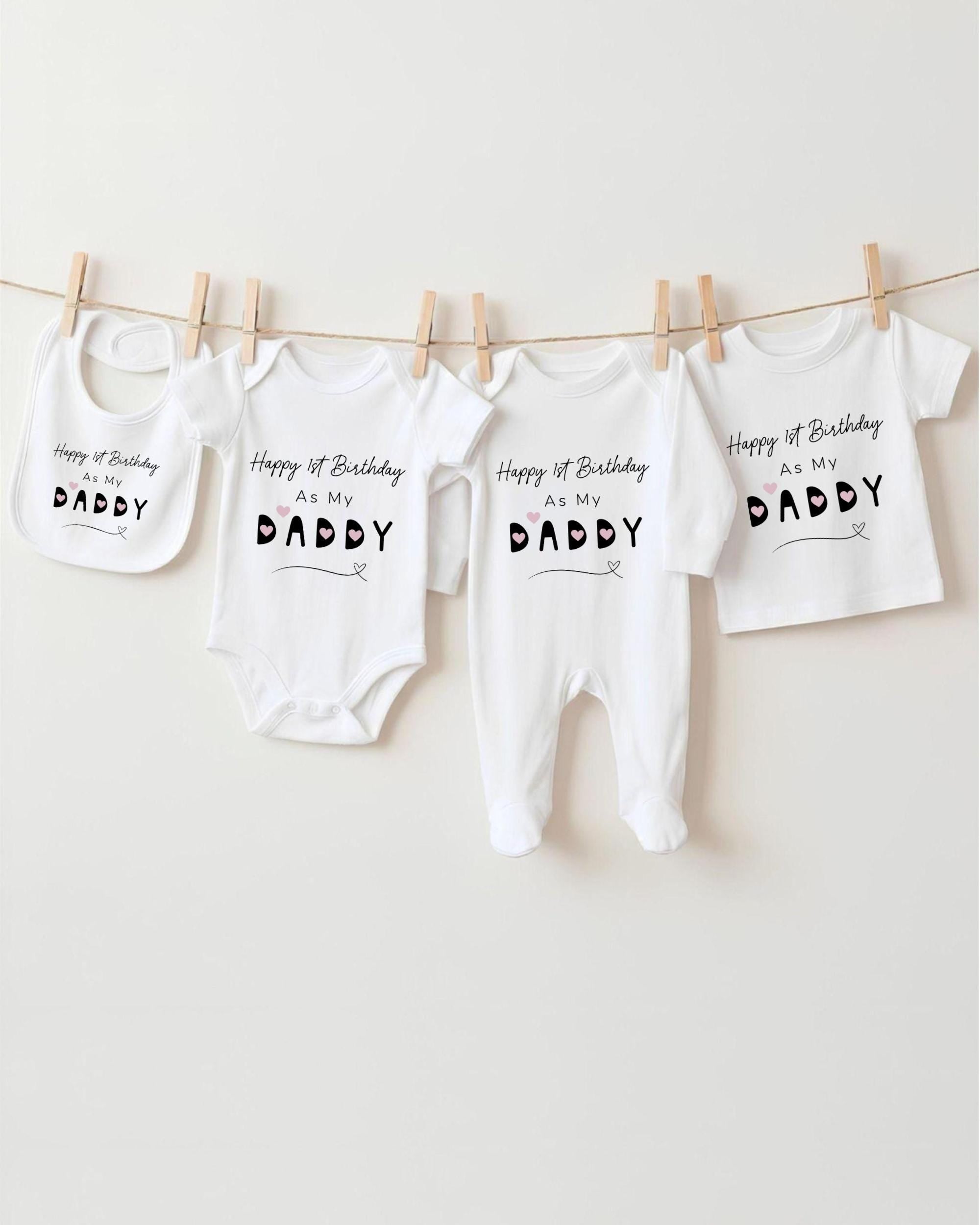 A row of white baby clothes with the text "Happy 1st Birthday as my DADDY" printed on them, hanging on a clothesline.