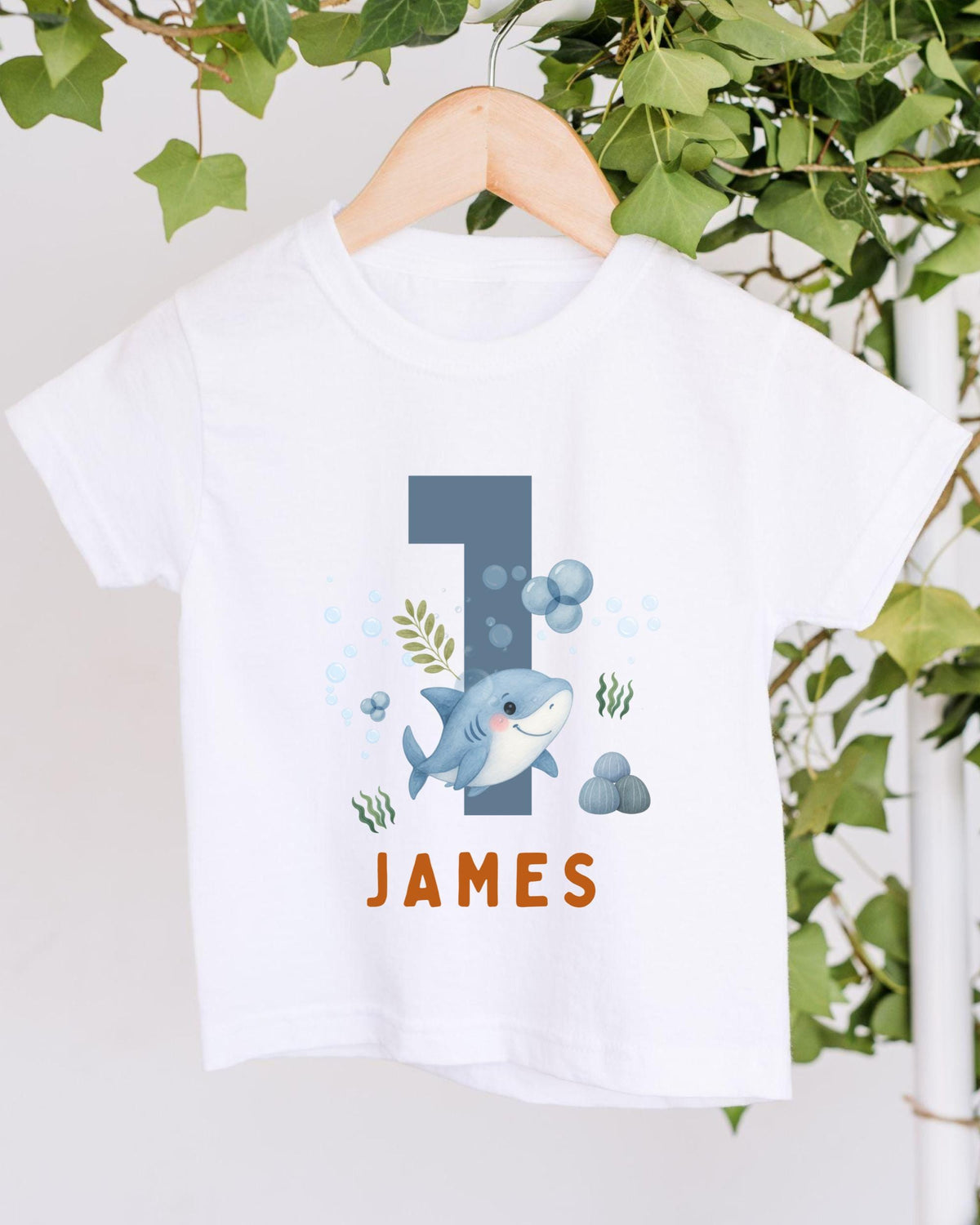 A white t-shirt with a graphic design featuring a shark and bubbles, along with the name "James" printed on it.