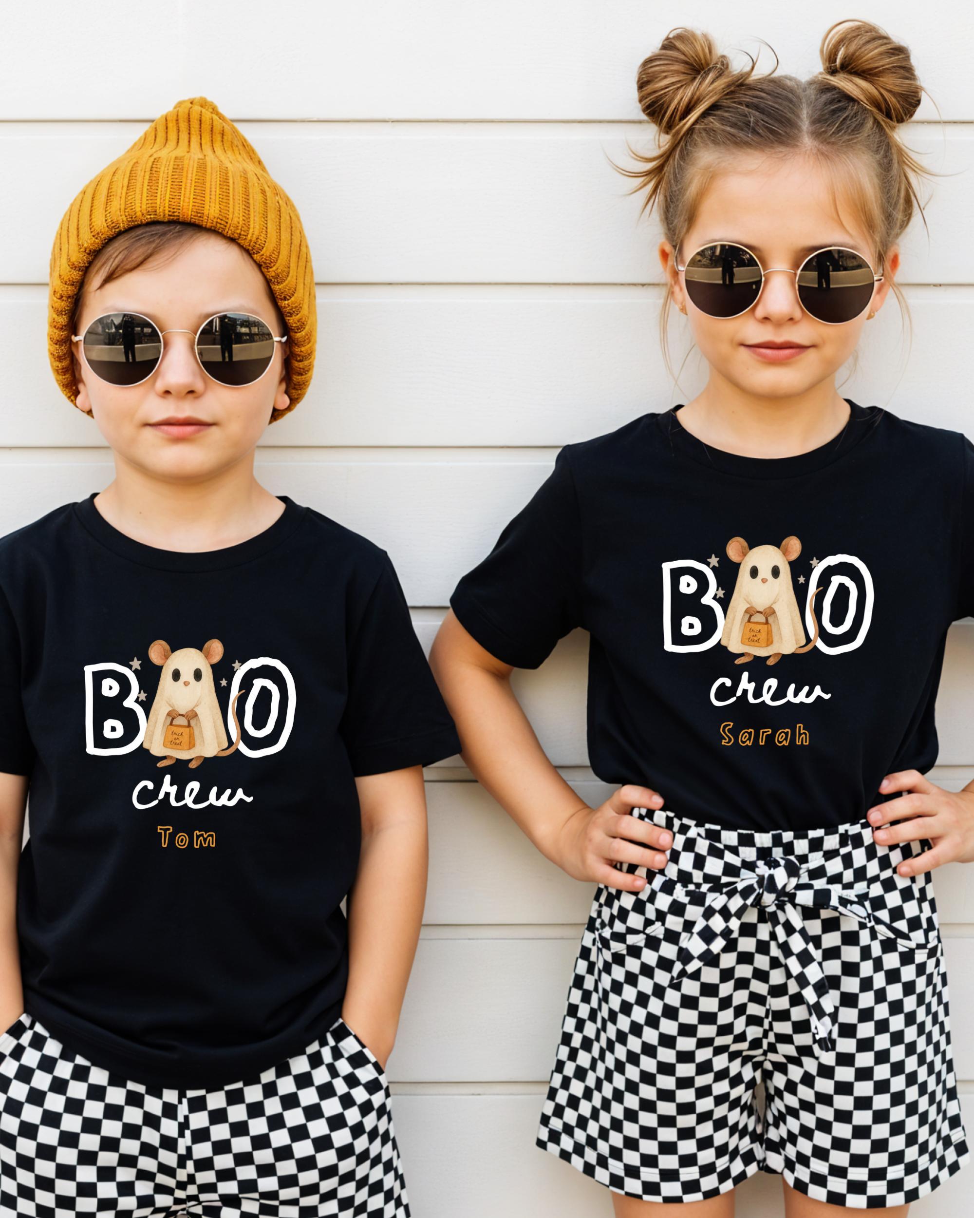 Two children wearing black t-shirts with a cartoon character and the text "BOO crew Tom" are standing against a white wall.