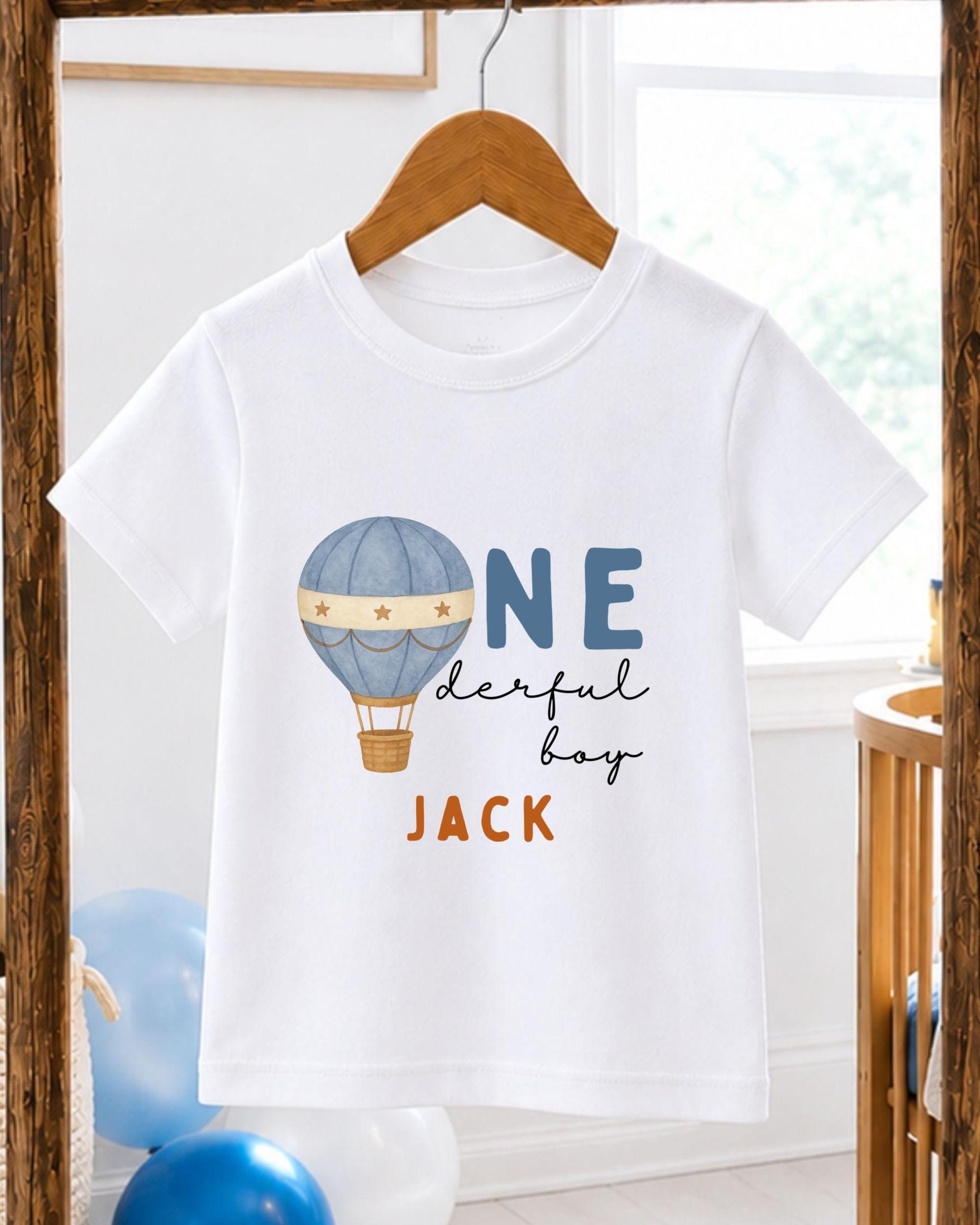 A white t-shirt with a graphic design of a hot air balloon and the text "ONE derful boy" printed on it.