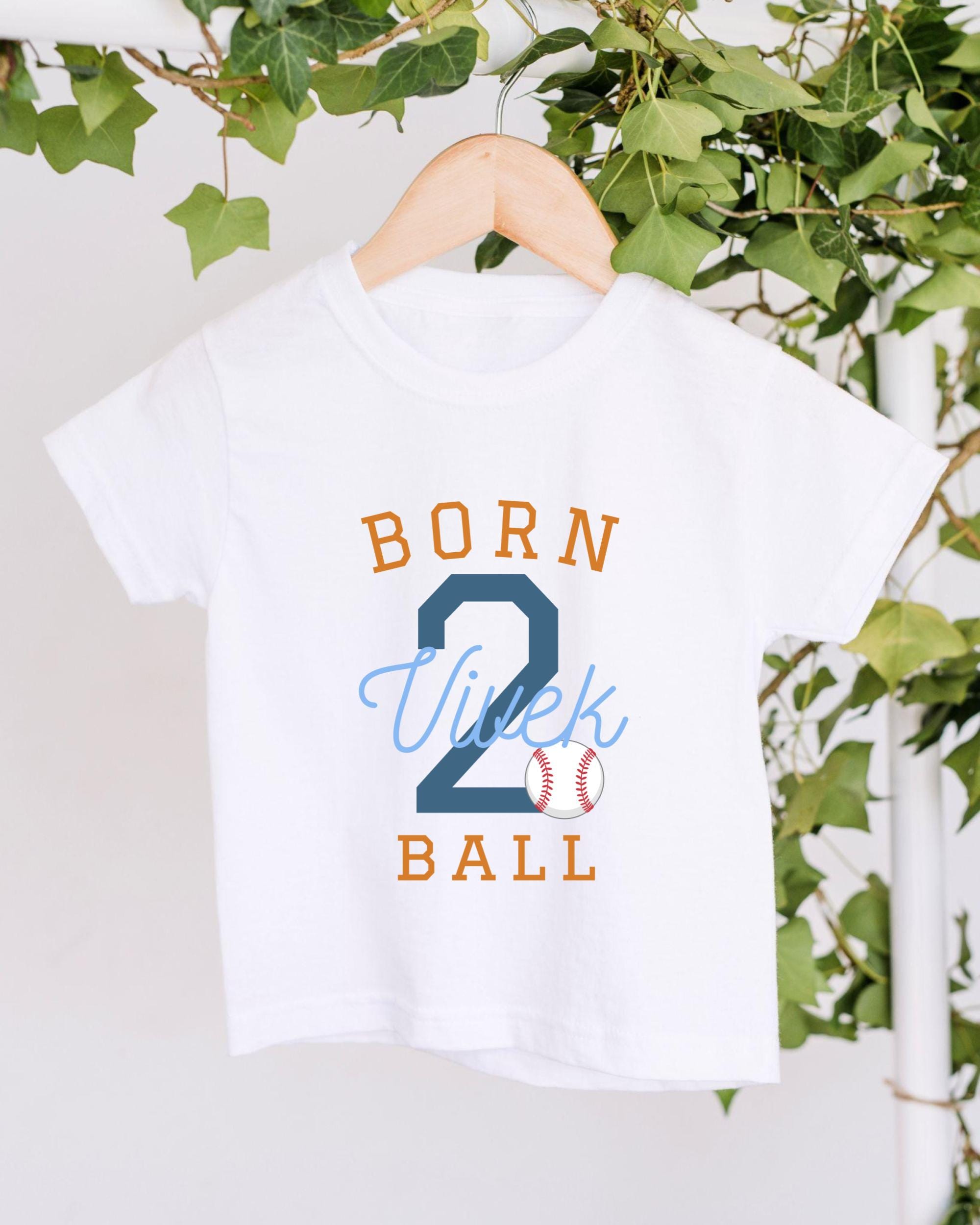 A white t-shirt with the text "BORN 2 BALL" printed on it, along with a baseball graphic.