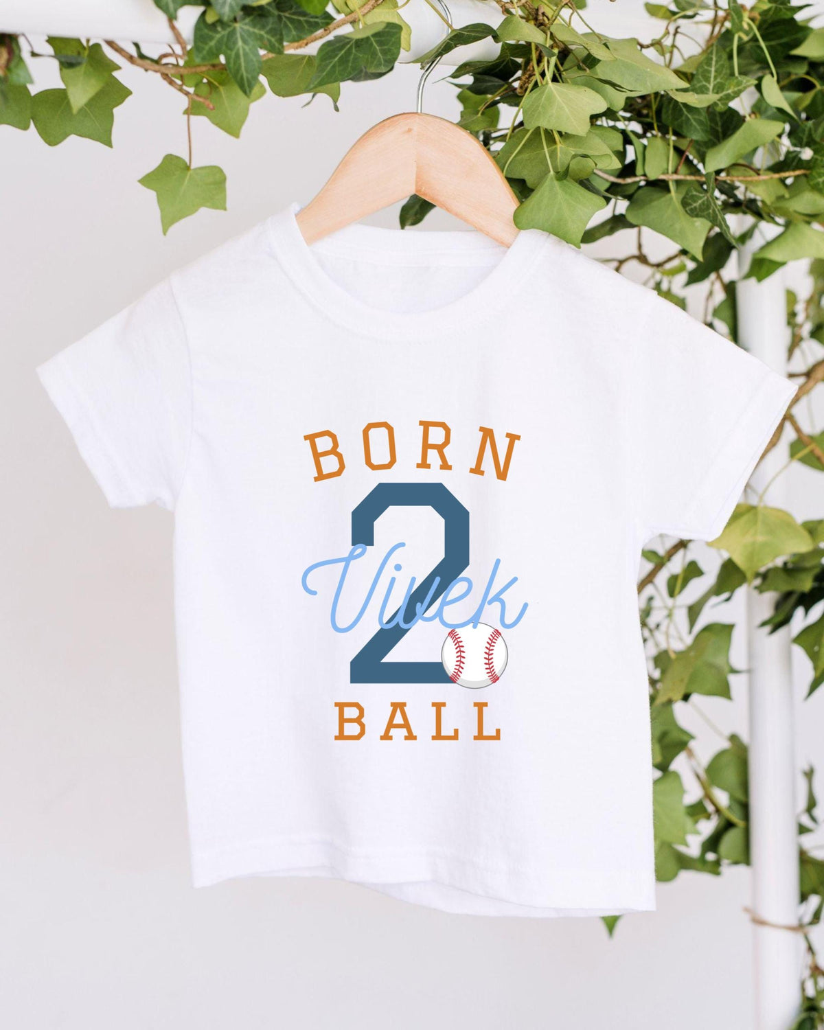 A white t-shirt with the text "BORN 2 BALL" printed on it, along with a baseball graphic.
