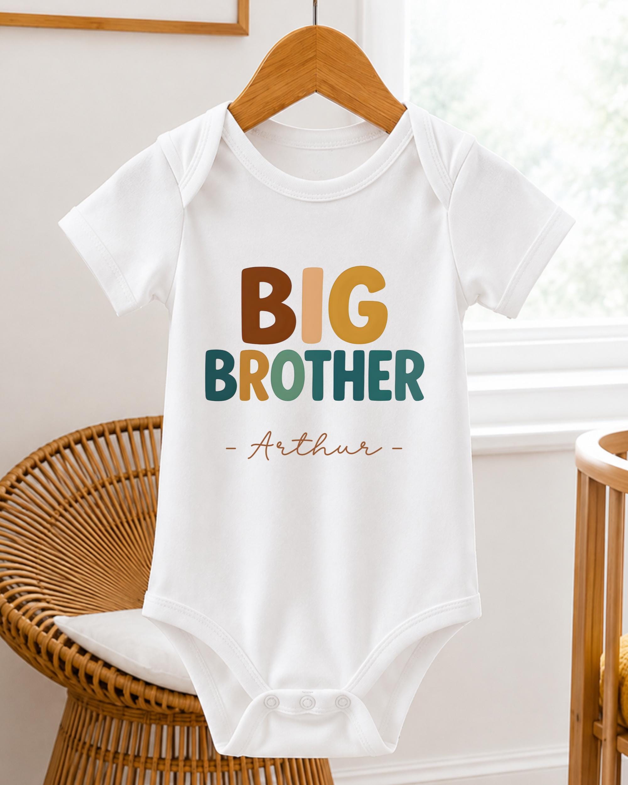 A white baby onesie with the text "BIG BROTHER Arthur" printed on it, hanging on a wooden hanger.