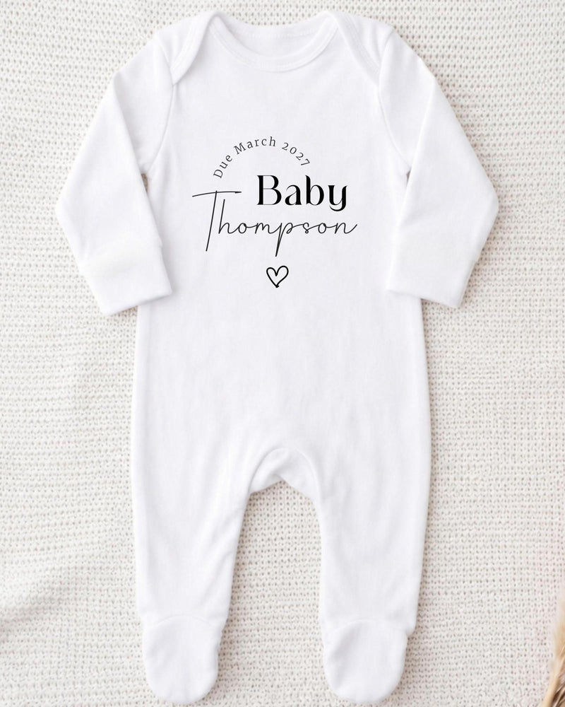 A white bodysuit with the text "Due March 2027 Baby Thompson" printed on it.