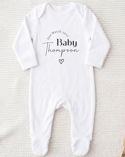 A white bodysuit with the text "Due March 2027 Baby Thompson" printed on it.