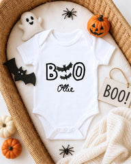 A white onesie with the text "BOO Olle" printed on it, surrounded by Halloween-themed decorations such as a ghost, a pumpkin, and bats.