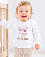 A smiling baby girl wearing a white sweater with text on it.