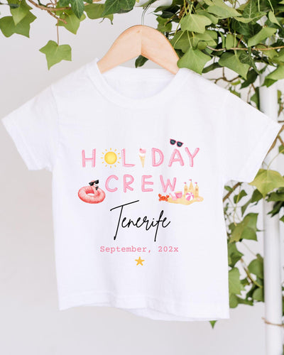 A white t-shirt with the text "HOLIDAY CREW Tenerife" printed on it, along with various summer-themed illustrations such as sunglasses, a beach ball, and a hot dog.