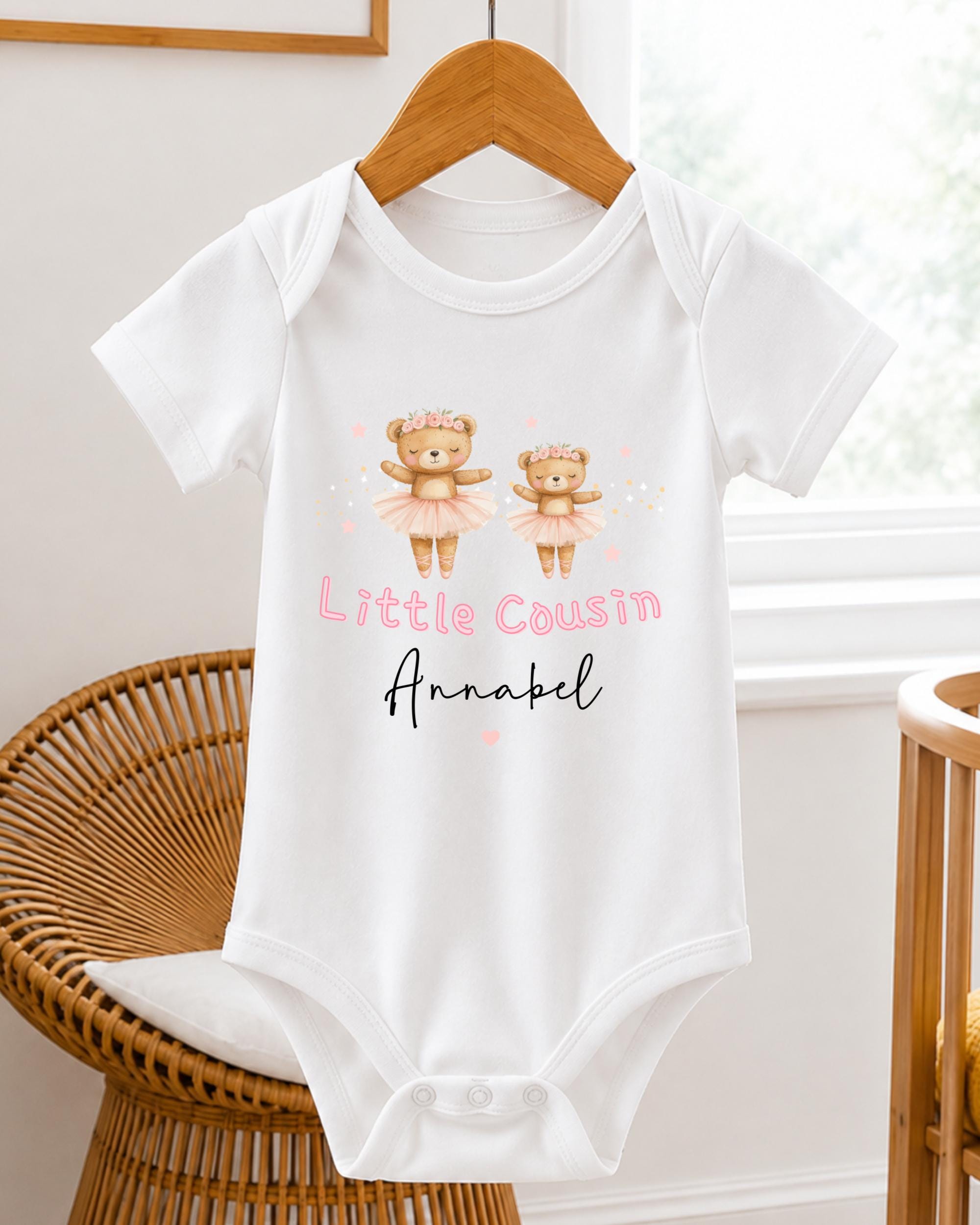 A white baby onesie with a design of two teddy bears in tutus and the text "Little Cousin Annabel" printed on it.