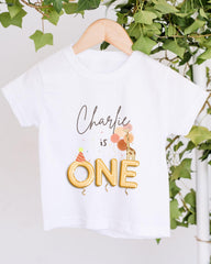 A white t-shirt with a personalized text and a graphic design, hanging on a wooden hanger.