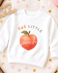 A white sweatshirt with a peach graphic and the text "ONE LITTLE peach" printed on it, surrounded by confetti.