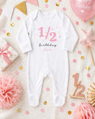 A white onesie with the number 1/2 and the text "Birthday Jane" printed on it, surrounded by confetti, a pink star, and other birthday decorations.
