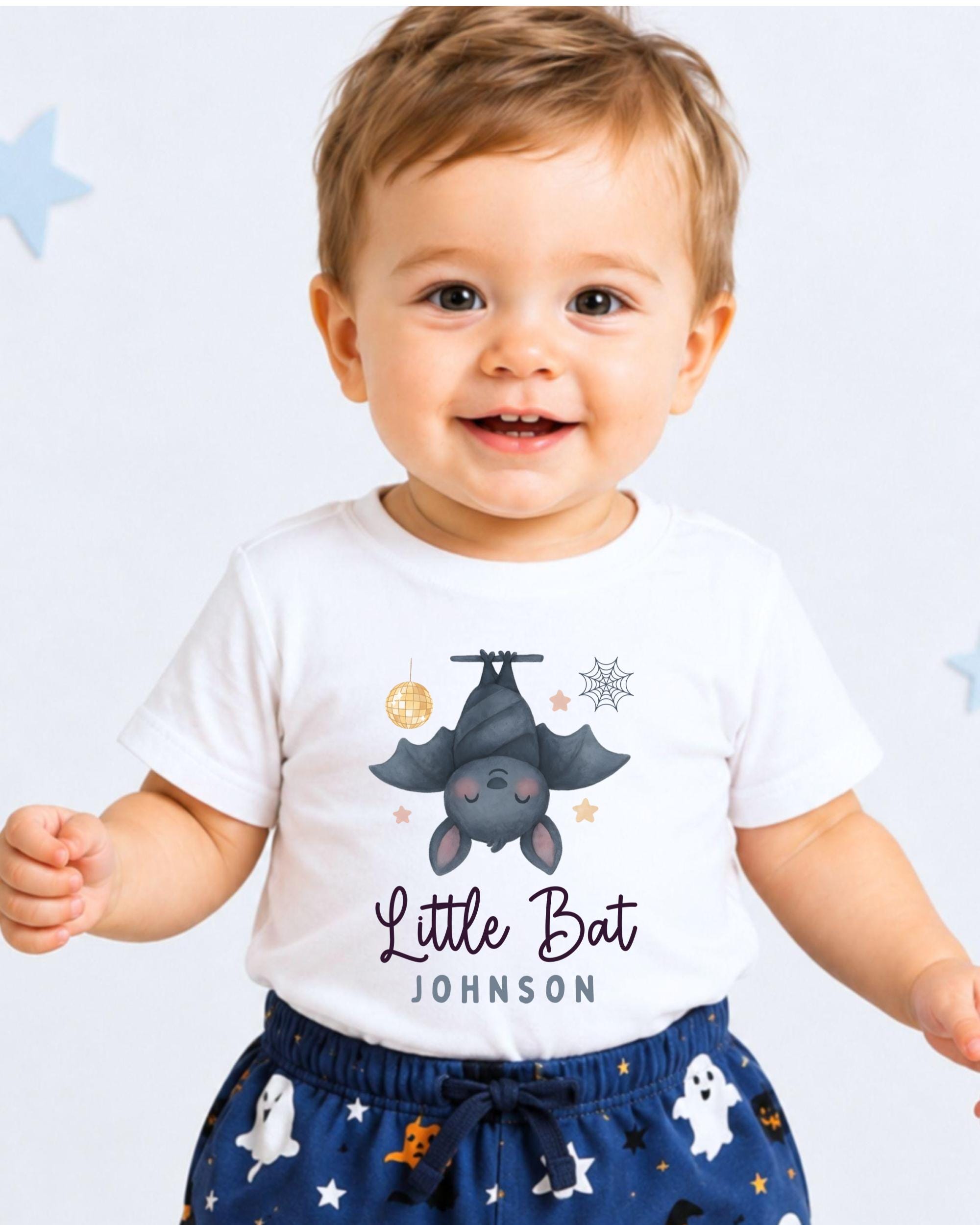 A smiling baby boy wearing a white t-shirt with a bat graphic and the text "Little Bat Johnson" printed on it.