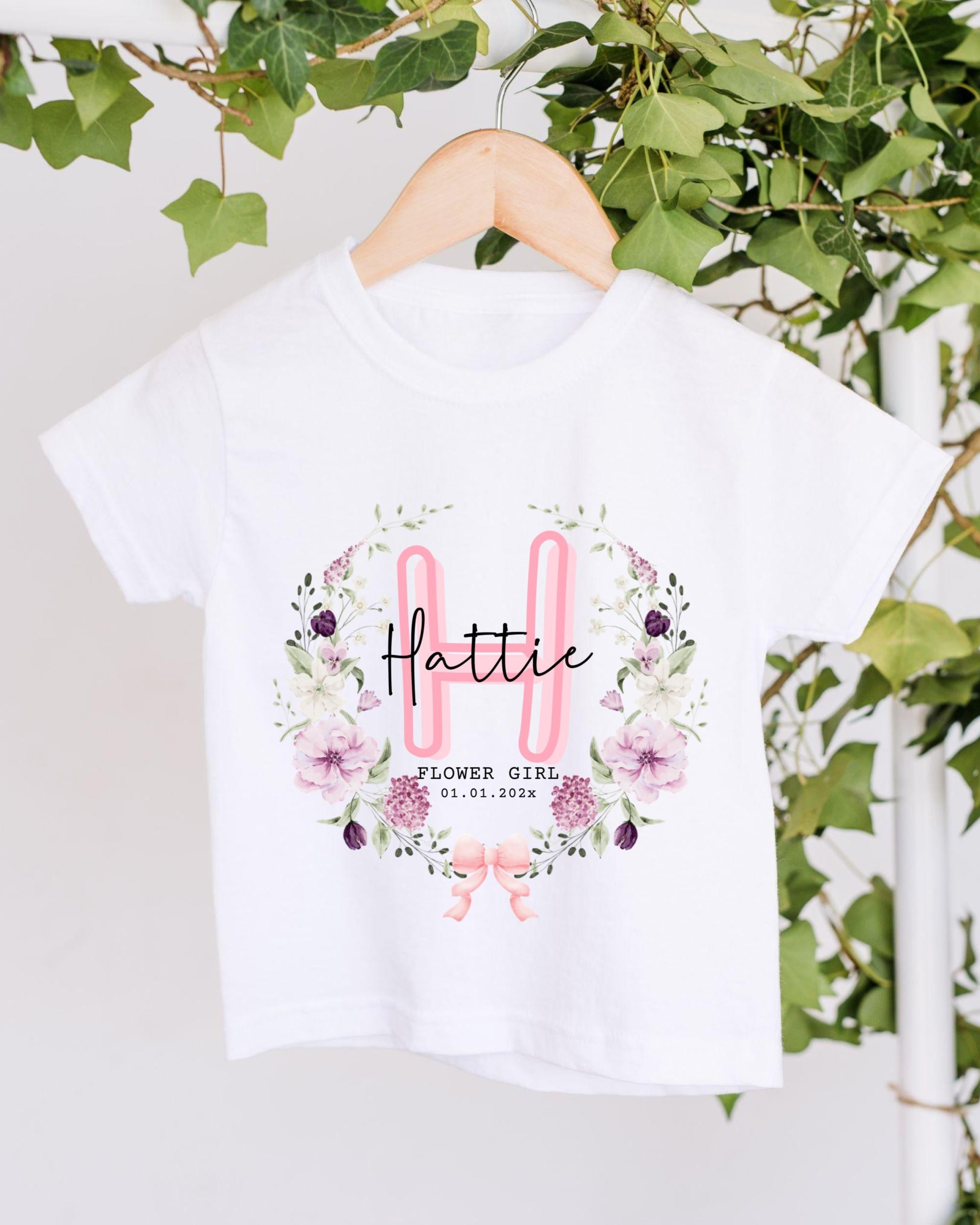 A white t-shirt with a floral design and text printed on it, hanging on a wooden hanger.