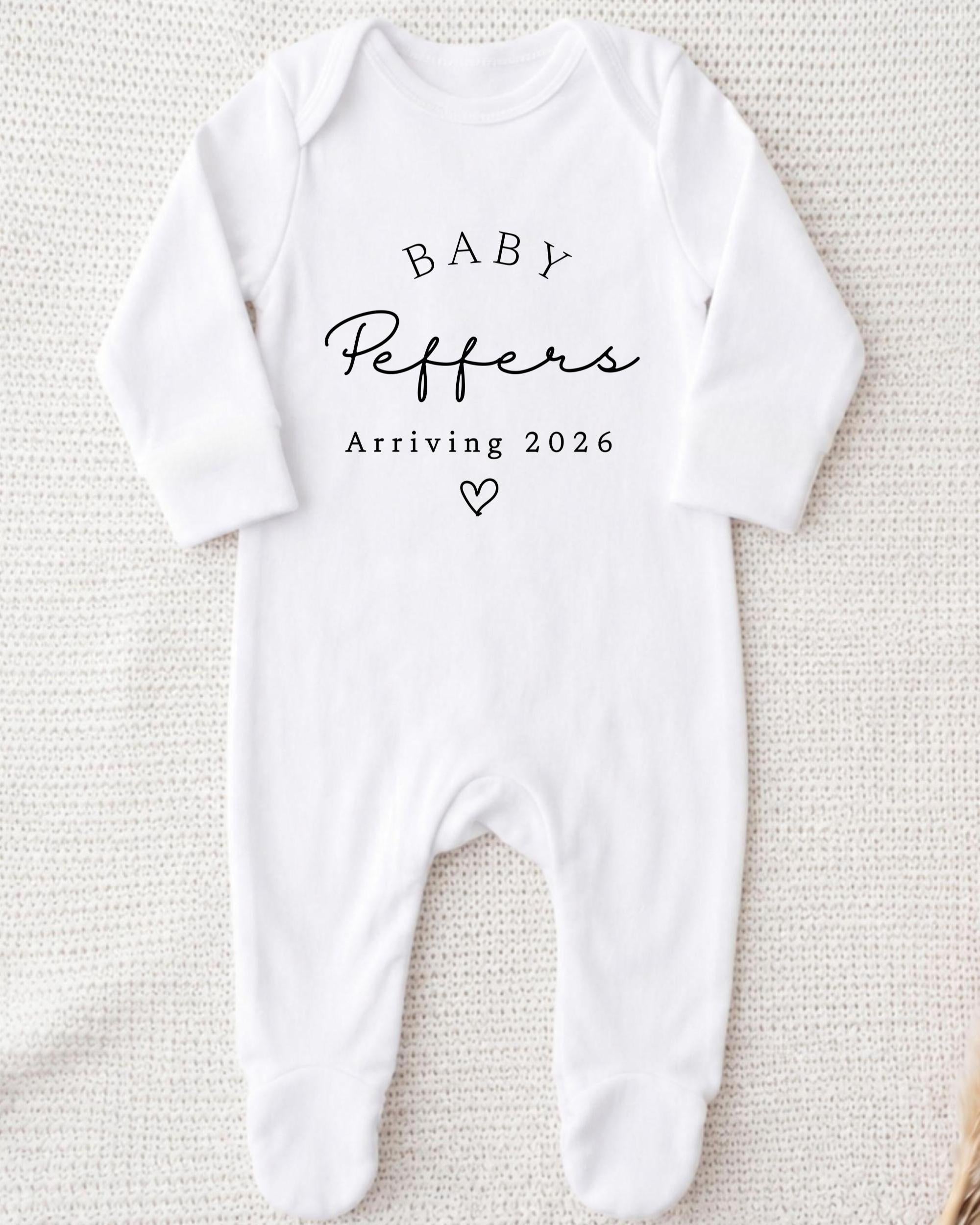 A white onesie with the text "BABY Peppers Arriving 2026" printed on it.