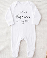 A white onesie with the text "BABY Peppers Arriving 2026" printed on it.