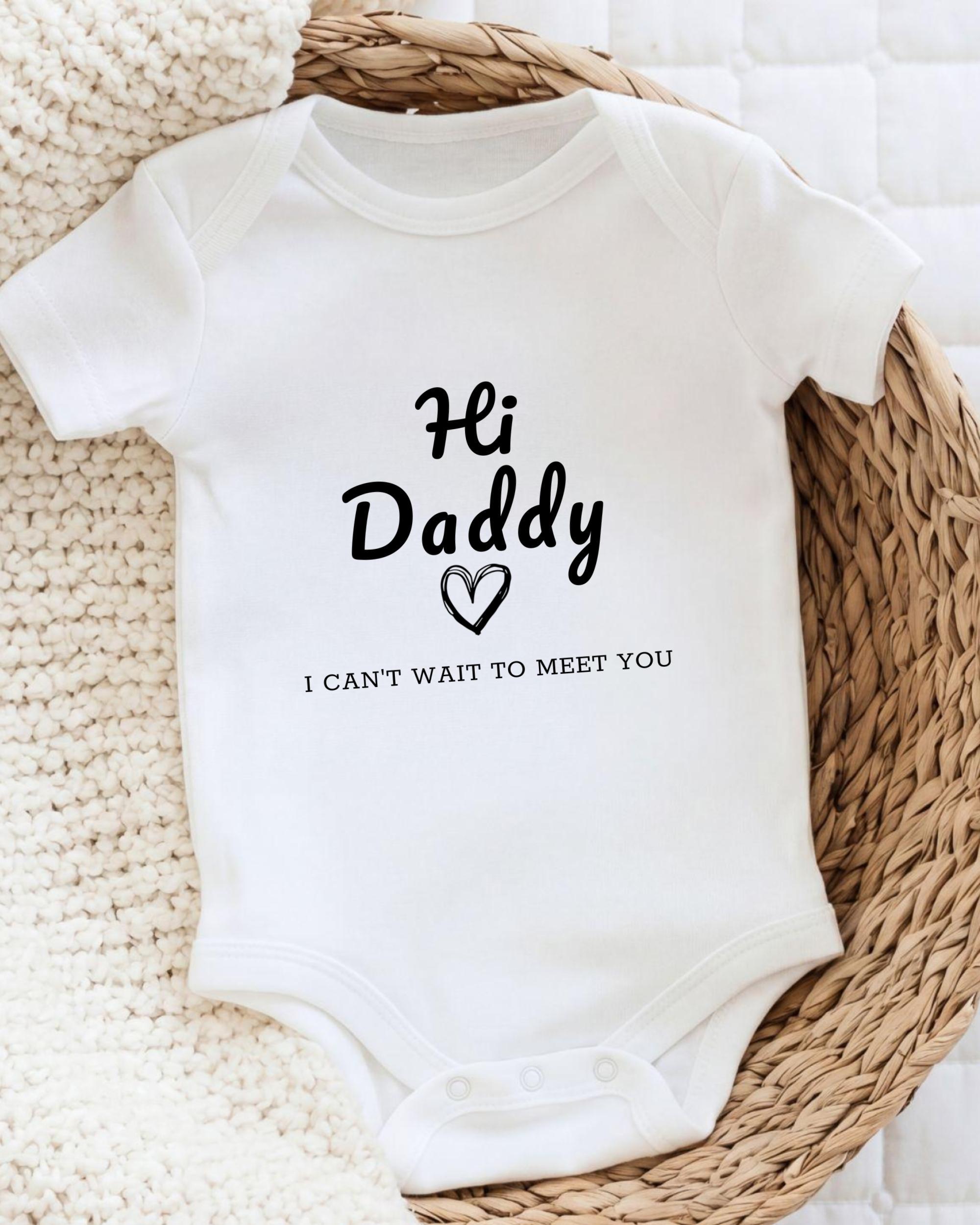 A white baby onesie with the text "Hi Daddy I can't wait to meet you" printed on it.