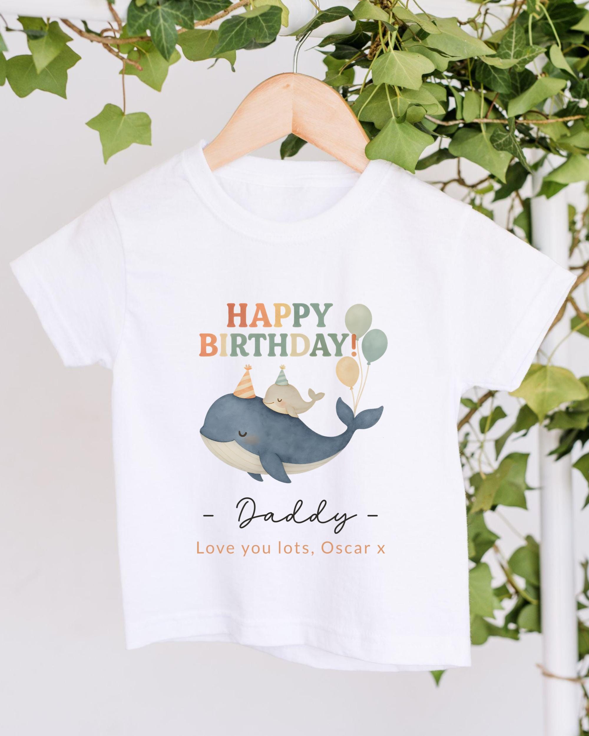 A white t-shirt with a graphic design of a whale and balloons, along with the text "Happy Birthday! Daddy - Love you lots, Oscar X".