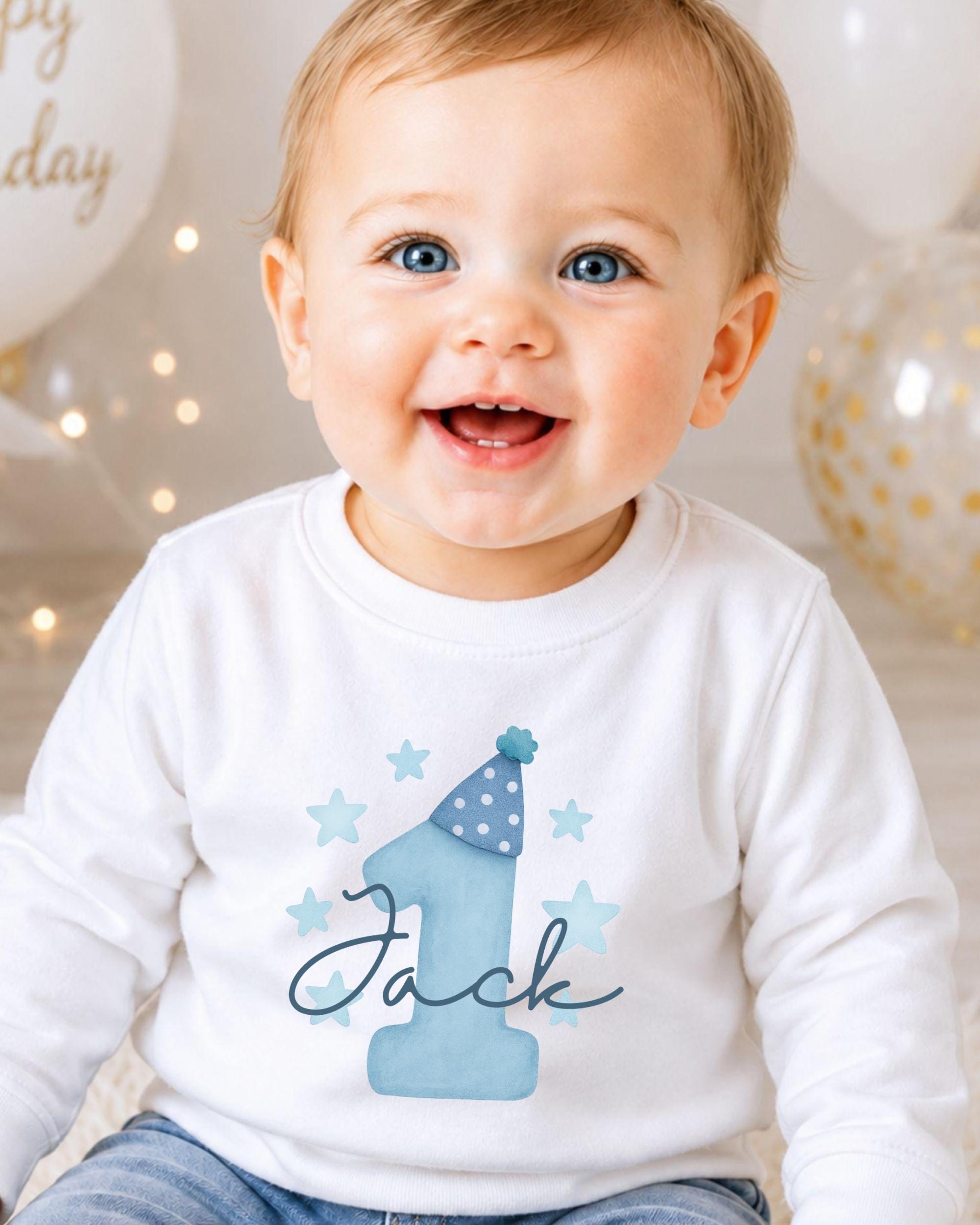 A smiling baby boy wearing a white shirt with a blue hat and stars, with the name "Jack" written on it.