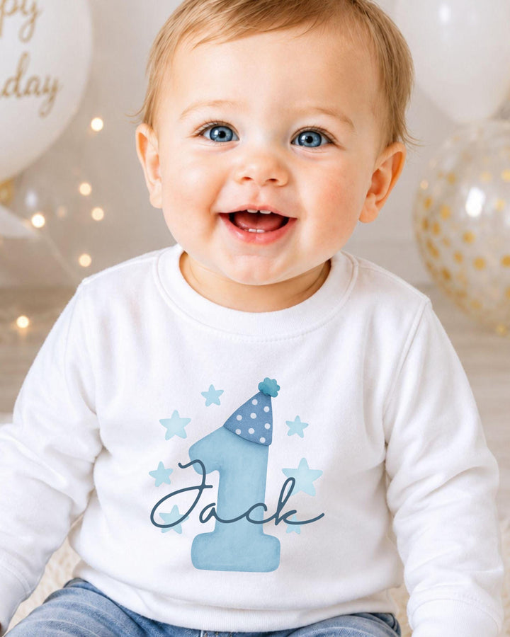 A smiling baby boy wearing a white shirt with a blue hat and stars, with the name "Jack" written on it.