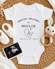A white baby onesie with text and an image of a baby, along with a crocheted rabbit toy and a baby bootie, all arranged on a woven placemat.