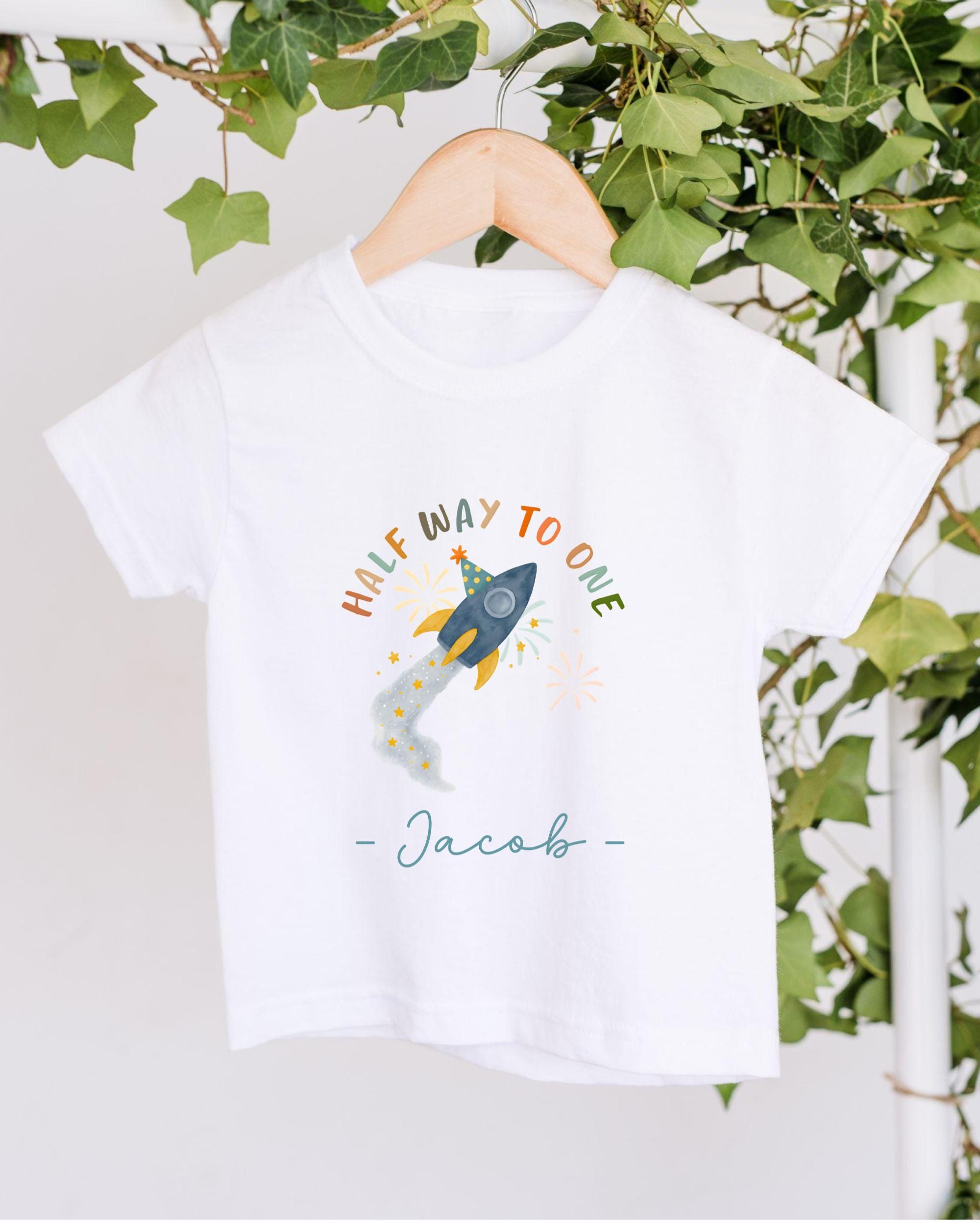A white t-shirt with a colorful graphic design and text, hanging on a wooden hanger.