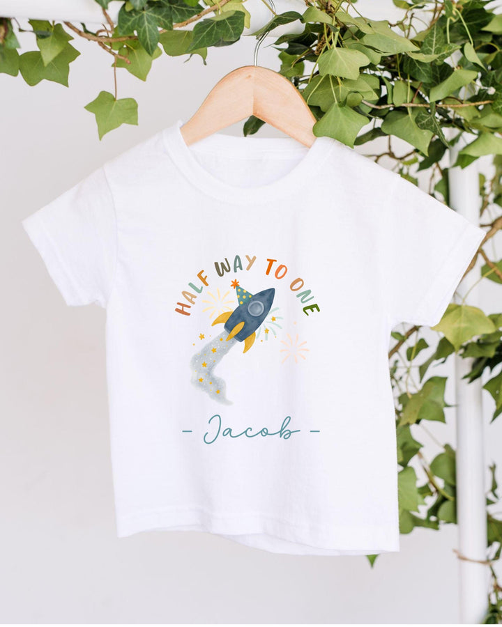 A white t-shirt with a colorful graphic design and text, hanging on a wooden hanger.