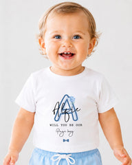 A smiling baby boy wearing a white t-shirt with a personalized message and a blue flower design.