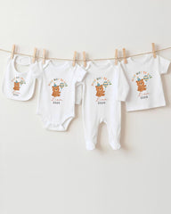 A collection of baby clothes, including onesies and bibs, hanging on a clothesline.