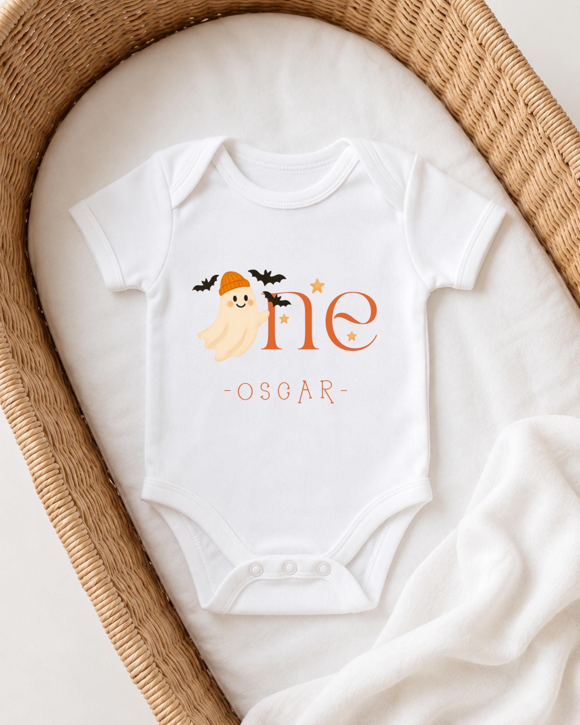 A white onesie with a ghost and the text "One Oscar" printed on it, placed in a wicker basket.