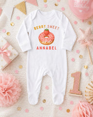 A white onesie with a pink donut and the text "Berry Sweet One Annabel" printed on it, surrounded by pink and gold confetti, a pink star, and a pink and gold birthday balloon.