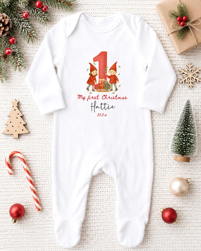 A white bodysuit with a red number 1 and a small illustration of two gnomes is displayed on a white background, surrounded by Christmas decorations and gifts.