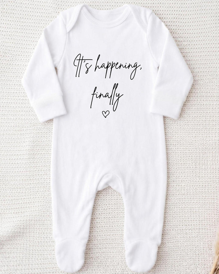 White Bib with black script 'It's happening, finally' and an outline heart for a IVF pregnancy announcement.