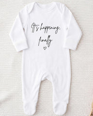 A white onesie with the text "It's happening, finally" printed on it.