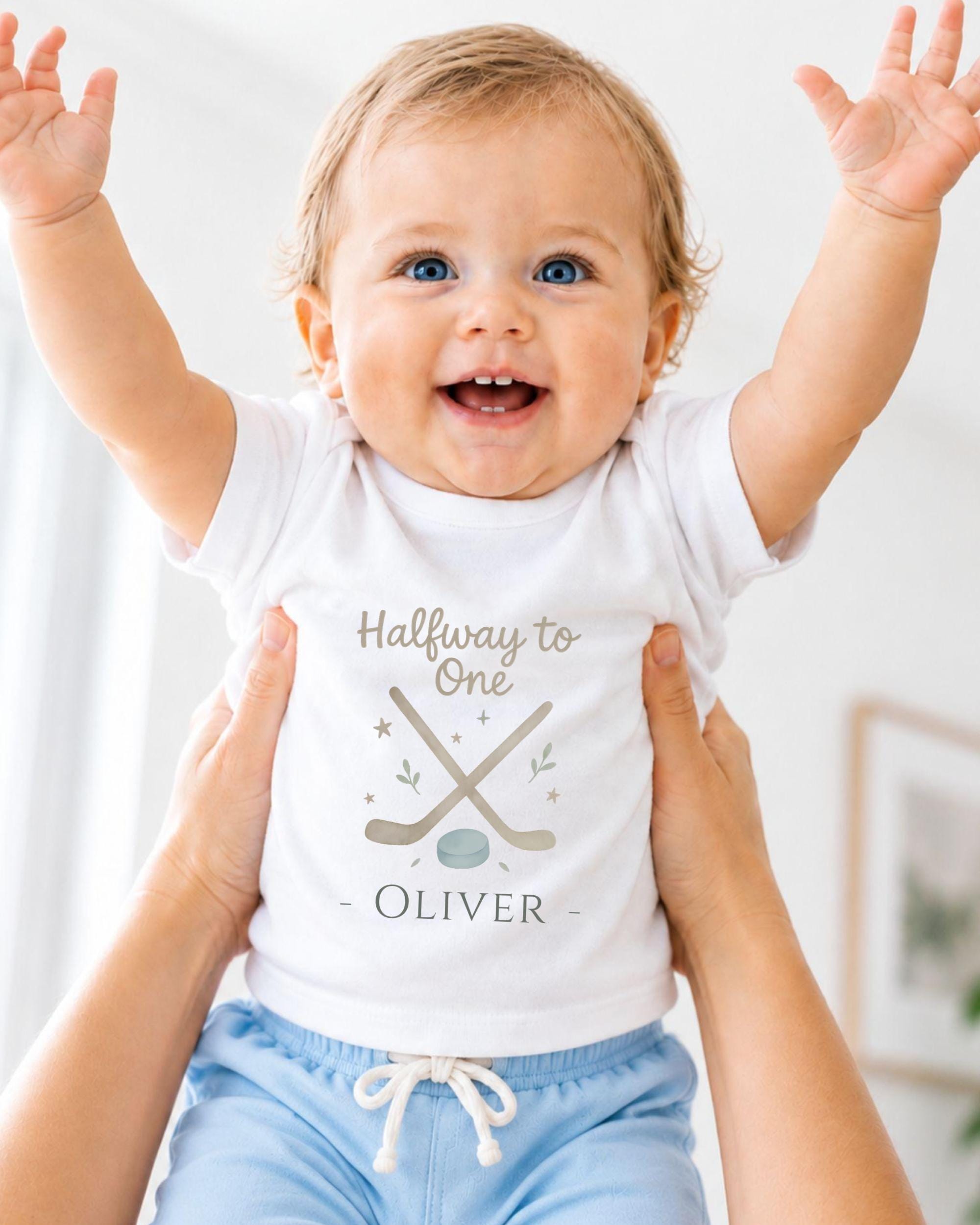 A smiling baby wearing a white t-shirt with the text "Halfway to One - Oliver" and a graphic of a hockey stick and puck.