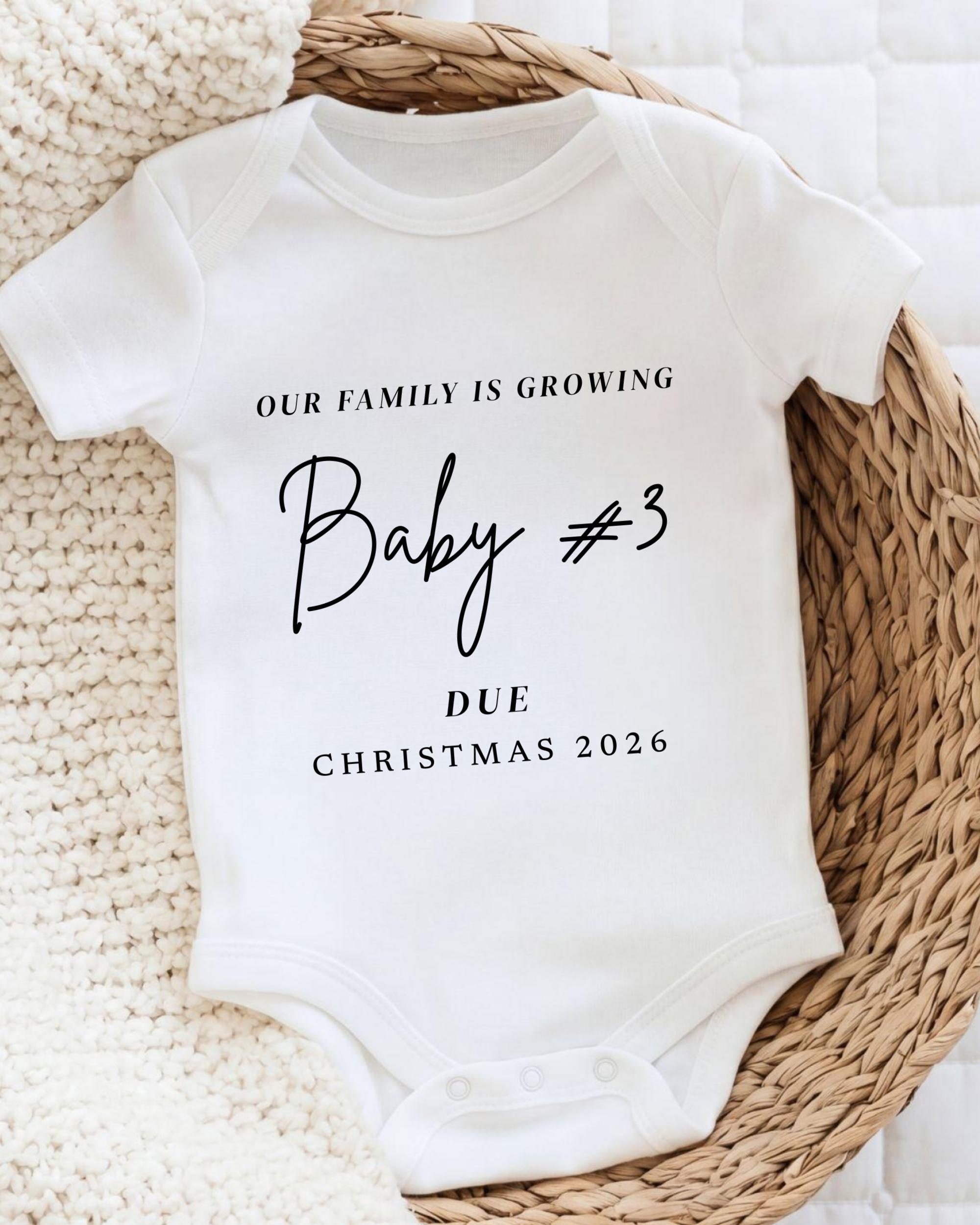 A white baby onesie with text printed on it, placed on a woven basket.