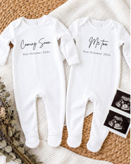 two white onesies with text and images related to a baby announcement.