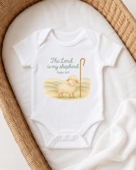 A white baby onesie with a Bible verse printed on it, resting on a white blanket.
