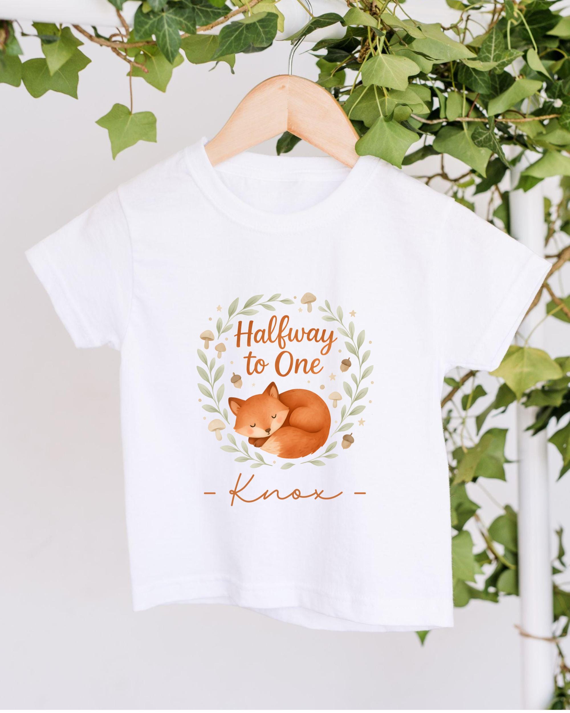 A white t-shirt with a graphic design featuring a sleeping fox and the text "Halfway to One" and "Knox" printed on it.