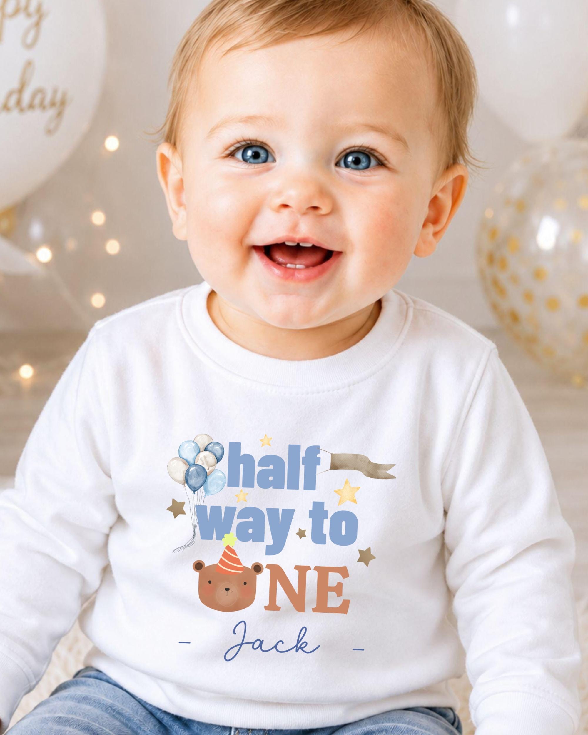 A smiling baby boy wearing a white shirt with a birthday message printed on it.