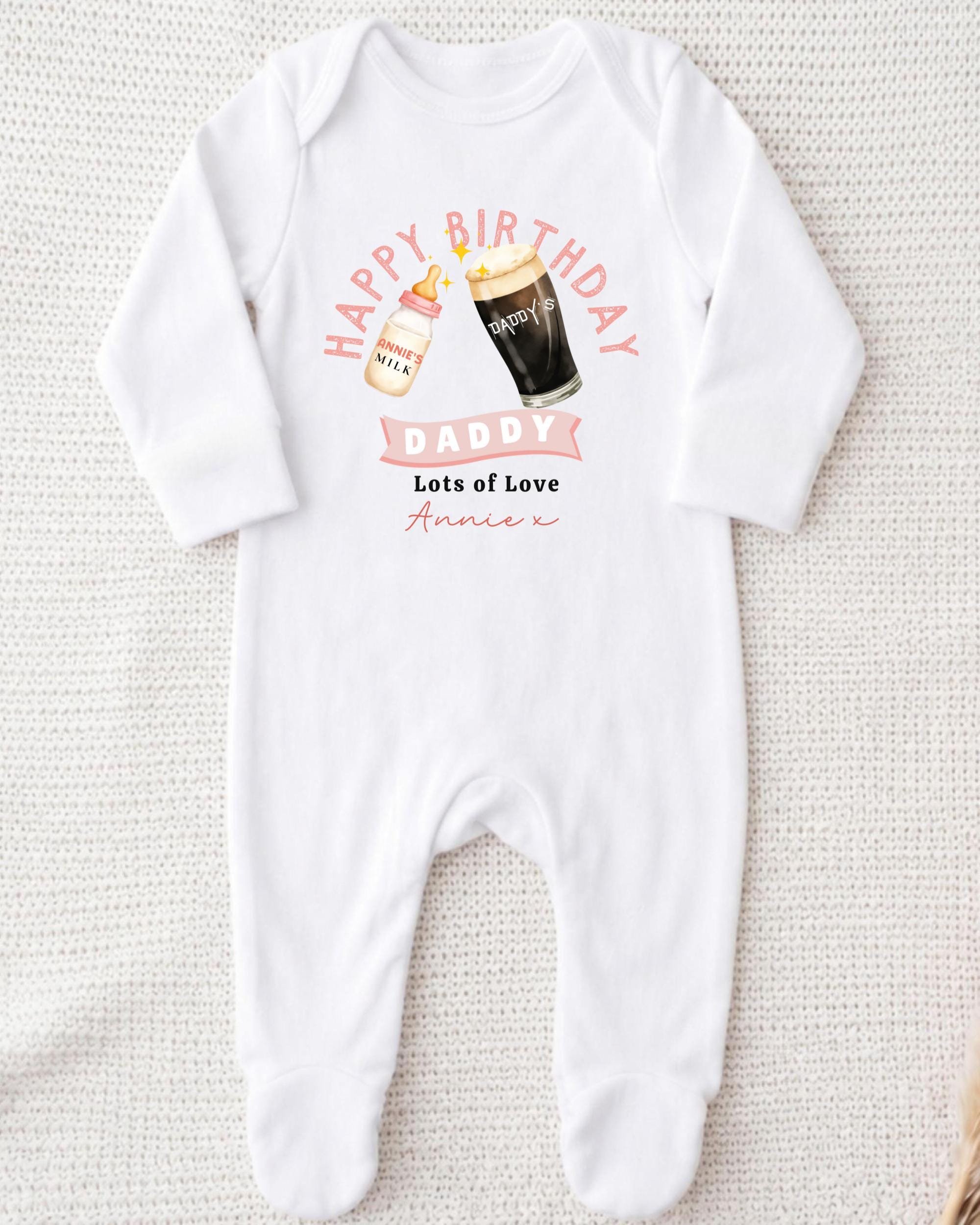 A white onesie with a graphic design on it, featuring a bottle of milk and a glass of beer, along with the text "Happy Birthday Daddy Lots of Love Annie" printed on it.